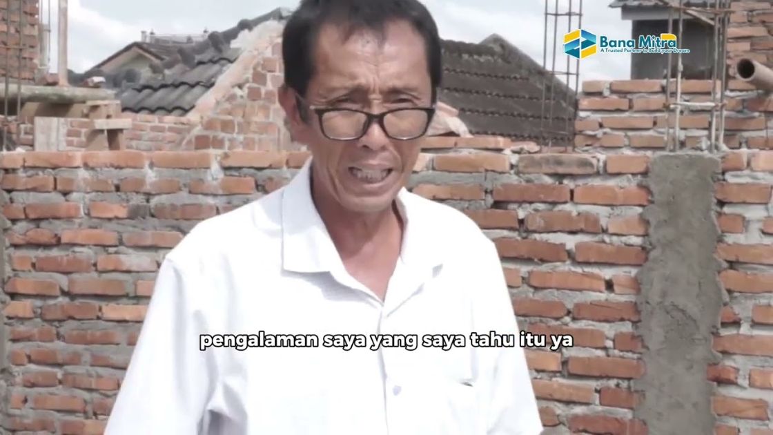 Seorang tukang Banamitra berbicara di depan dinding bata yang sedang dikerjakan di lokasi proyek